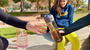 Hand passing Big Black Tea Bottle to another lighter vanilla Hand 